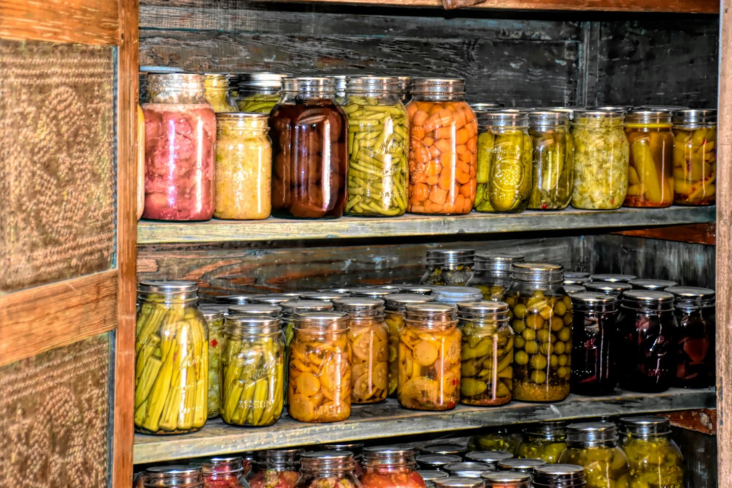 Home-canned fruits, vegetables, and pickles in glass jars on wooden shelves.